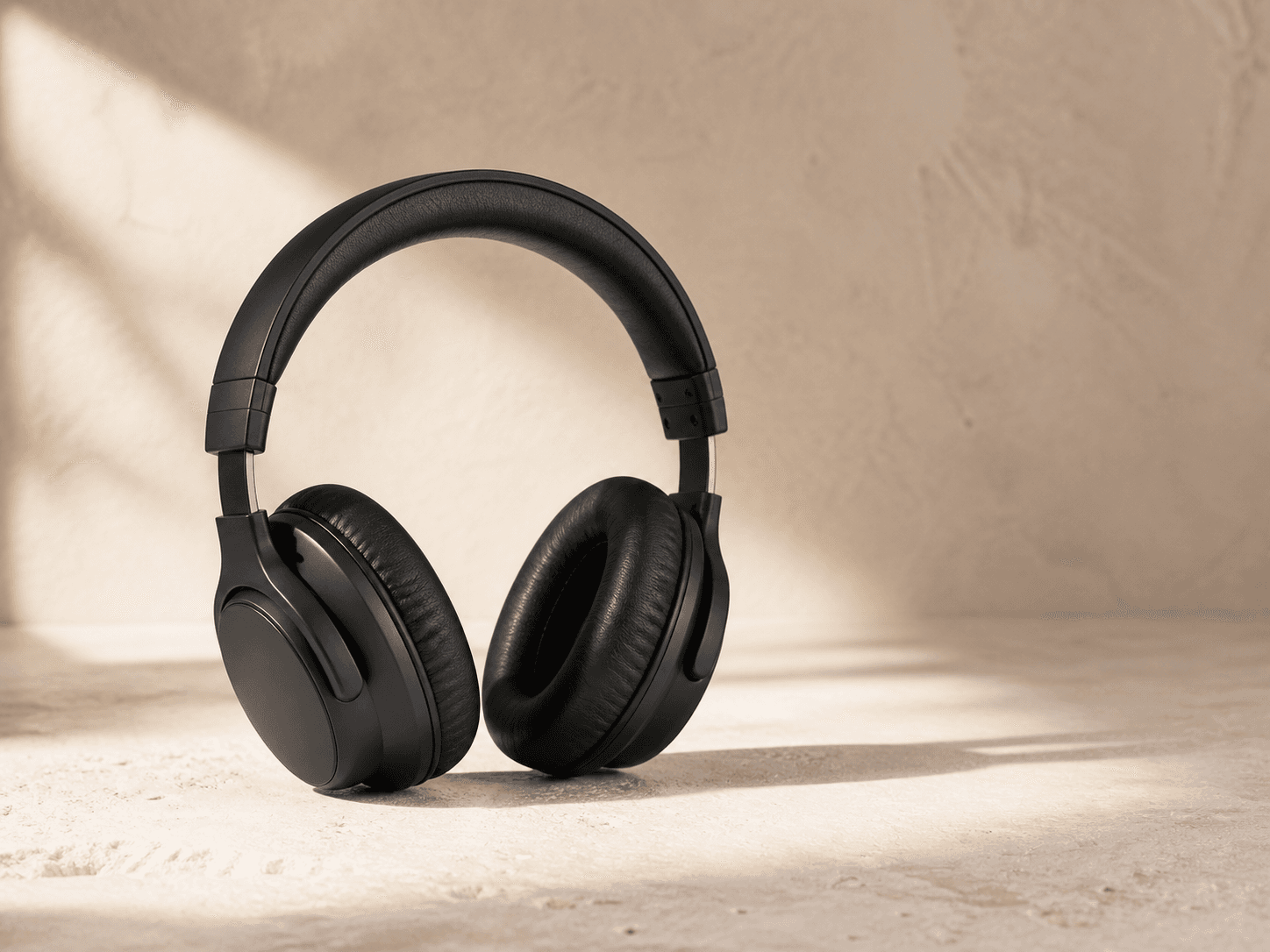 Unbranded black wireless headphones on a warm limestone surface.