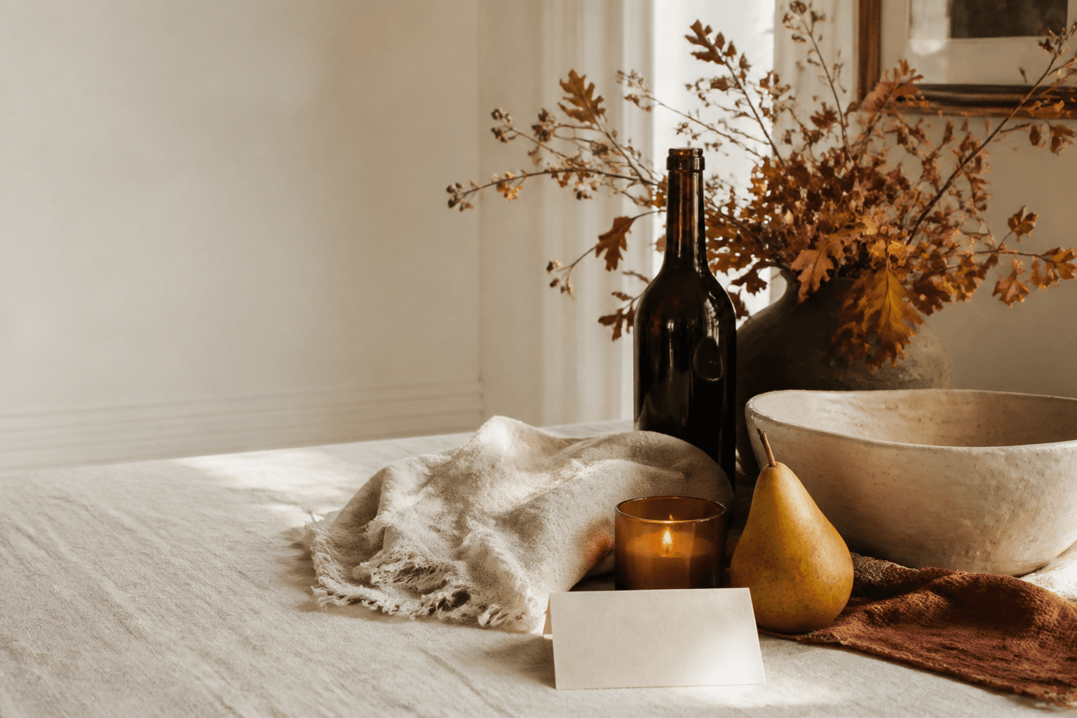A bottle, candle, pear, linen and handmade ceramics arranged for a Thanksgiving table.
